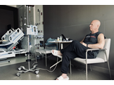 Howard Aaron sits in an armchair in his patient room, next to an IV pole. 